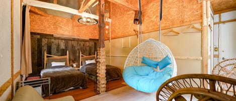 Una habitación rústica con techo de madera, un sillón colgante, una cama con cabecero y una pared blanca.