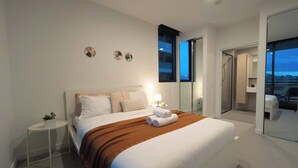 Une chambre d’hôtel moderne avec un grand lit, une petite table de chevet, une commode, un miroir et une vue sur l’extérieur.