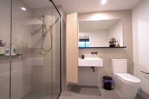 Ein modernes Badezimmer mit Duschkabine aus Glas, einem weißen Waschbecken, einer Toilette und einem Spiegel über dem Waschbecken.