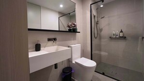 Uma casa de banho moderna com cabine de duche em vidro, lavatório branco e sanita.
