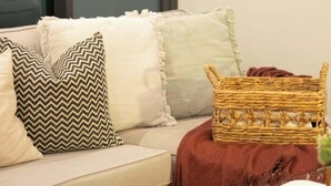 Un salon avec un canapé, des coussins, un panier en osier et une petite table sur laquelle se trouve une assiette.