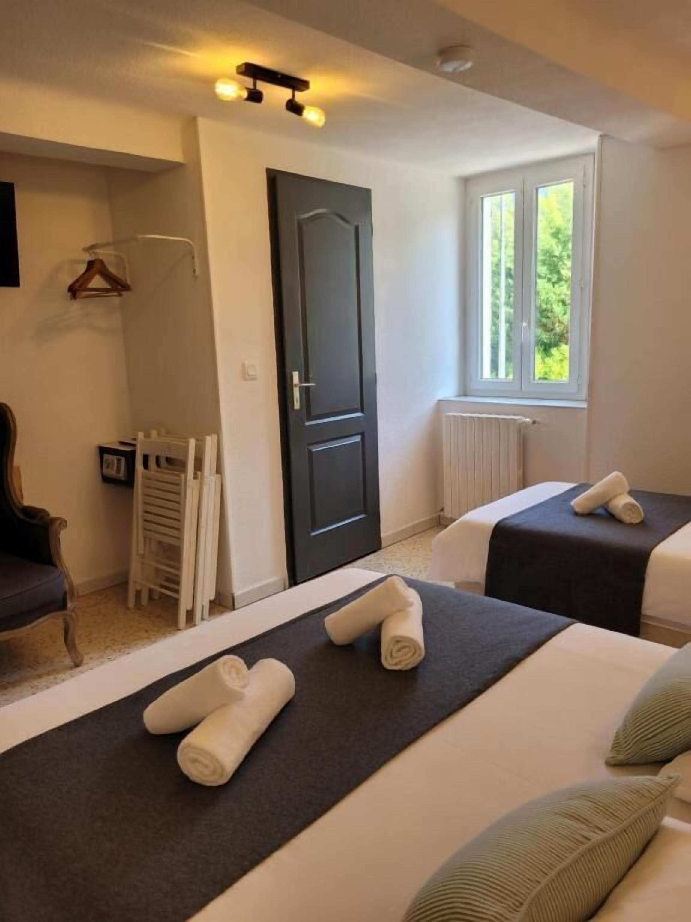 A hotel room with two beds, a dark door, a window with a view of greenery, and a radiator.