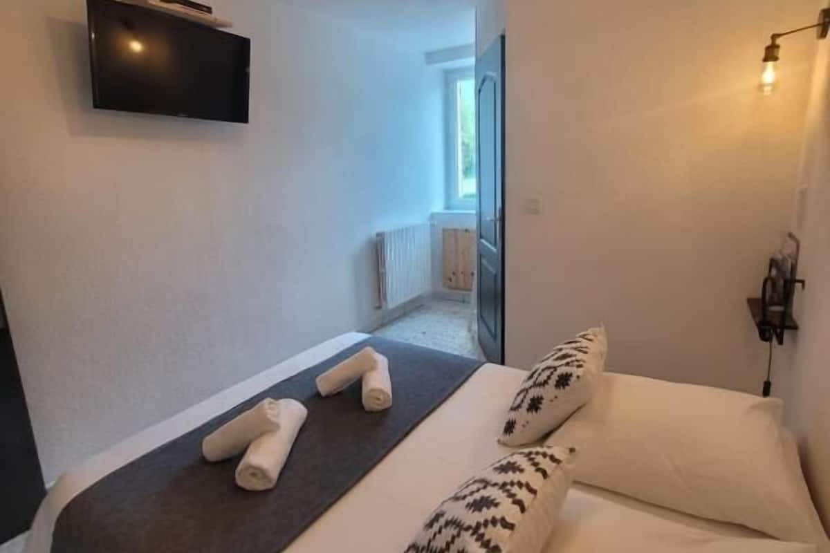 A bedroom with a bed, pillows, a TV, and a ceiling light fixture.