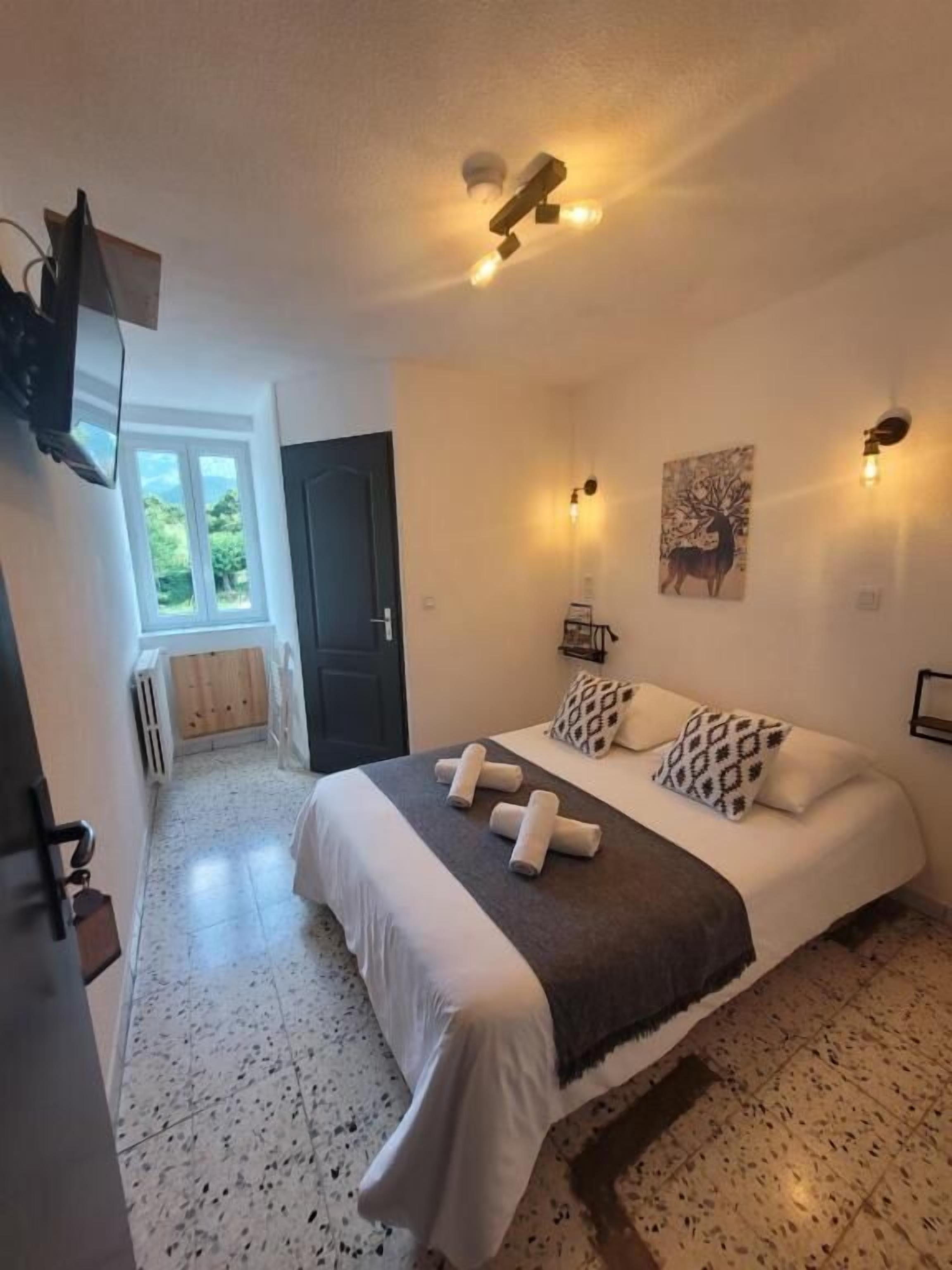 A bedroom with a bed, a wall-mounted TV, a door, and a window.