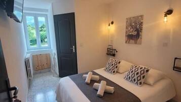 A bedroom with a bed, a wall-mounted TV, a door, and a window.