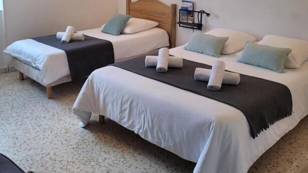 A hotel room with two single beds, each with a wooden headboard, white bedding, and a small bedside table. - L'étape (Les Omergues)
