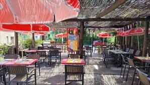 An outdoor patio with tables and chairs, red umbrellas, and a wooden pergola structure. - L'étape (Les Omergues)