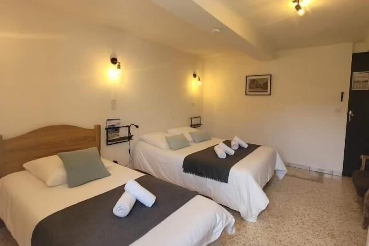 A hotel room with two beds, a wooden headboard, a small table, and a door.