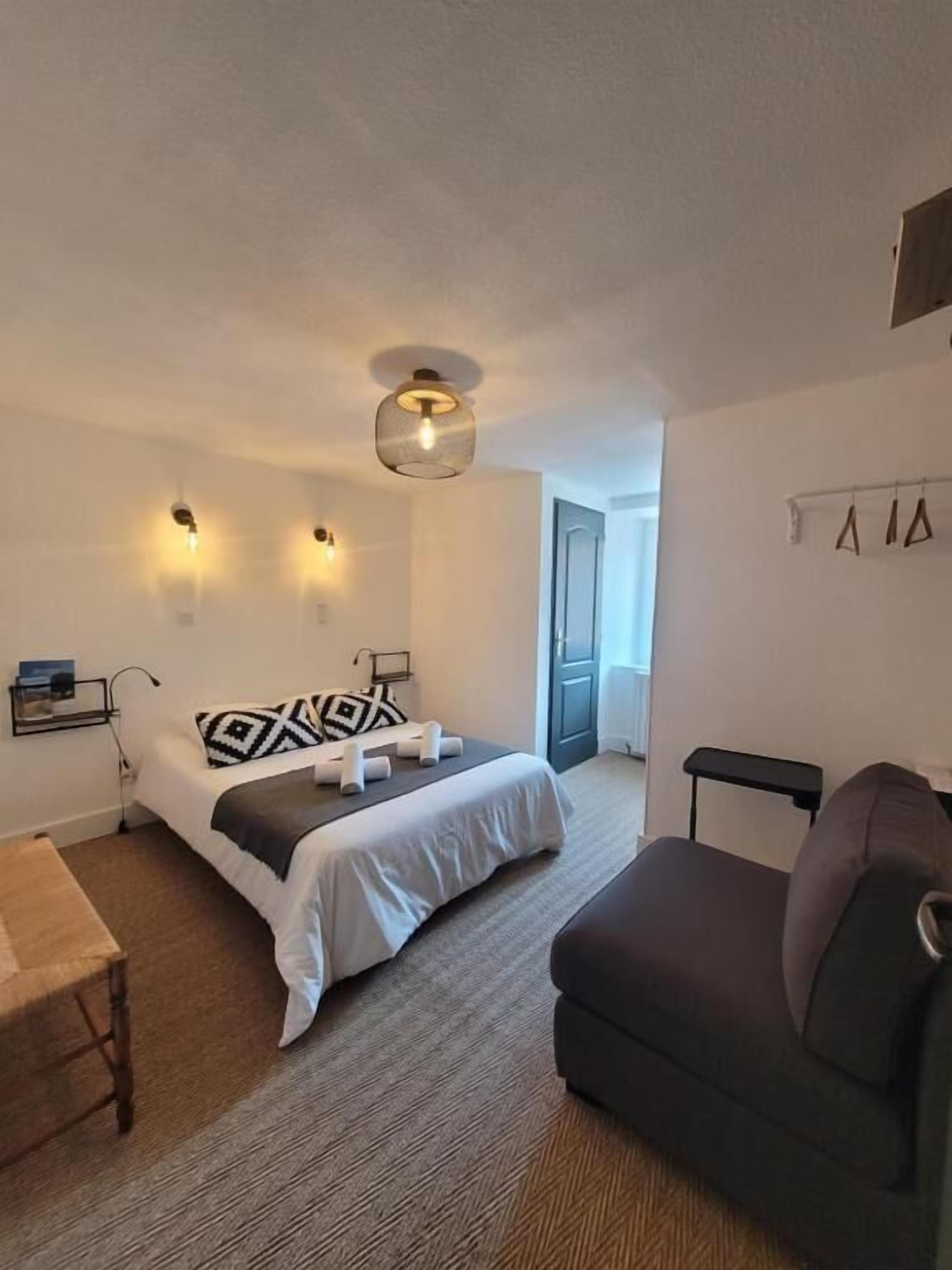 A bedroom with a bed, a sofa, a small table, and a wall-mounted shelf.