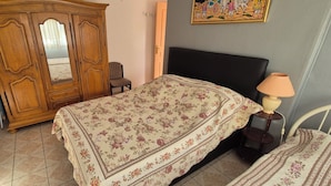 A bedroom with a bed, a chair, a wooden wardrobe, and a lamp.