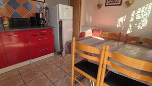 A kitchen with red cabinets, a white refrigerator, a coffee maker, and a dining table with a patterned tablecloth.