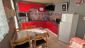 A compact kitchen with red cabinets, a microwave, a toaster, and a refrigerator.