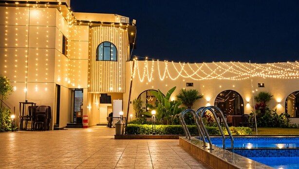 Un edificio con un letrero que dice 'Nakshatra Aura', una zona de piscina y luces colgantes.