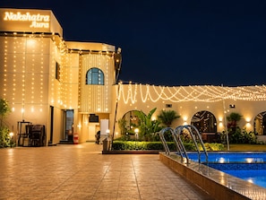 A building with a sign reading 'Nakshatra Aura,' a pool area, and string lights. - Nakshatra Aura (Indore)