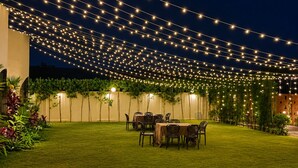 Un espacio exterior bien iluminado con luces colgantes, un césped y una zona de comedor.