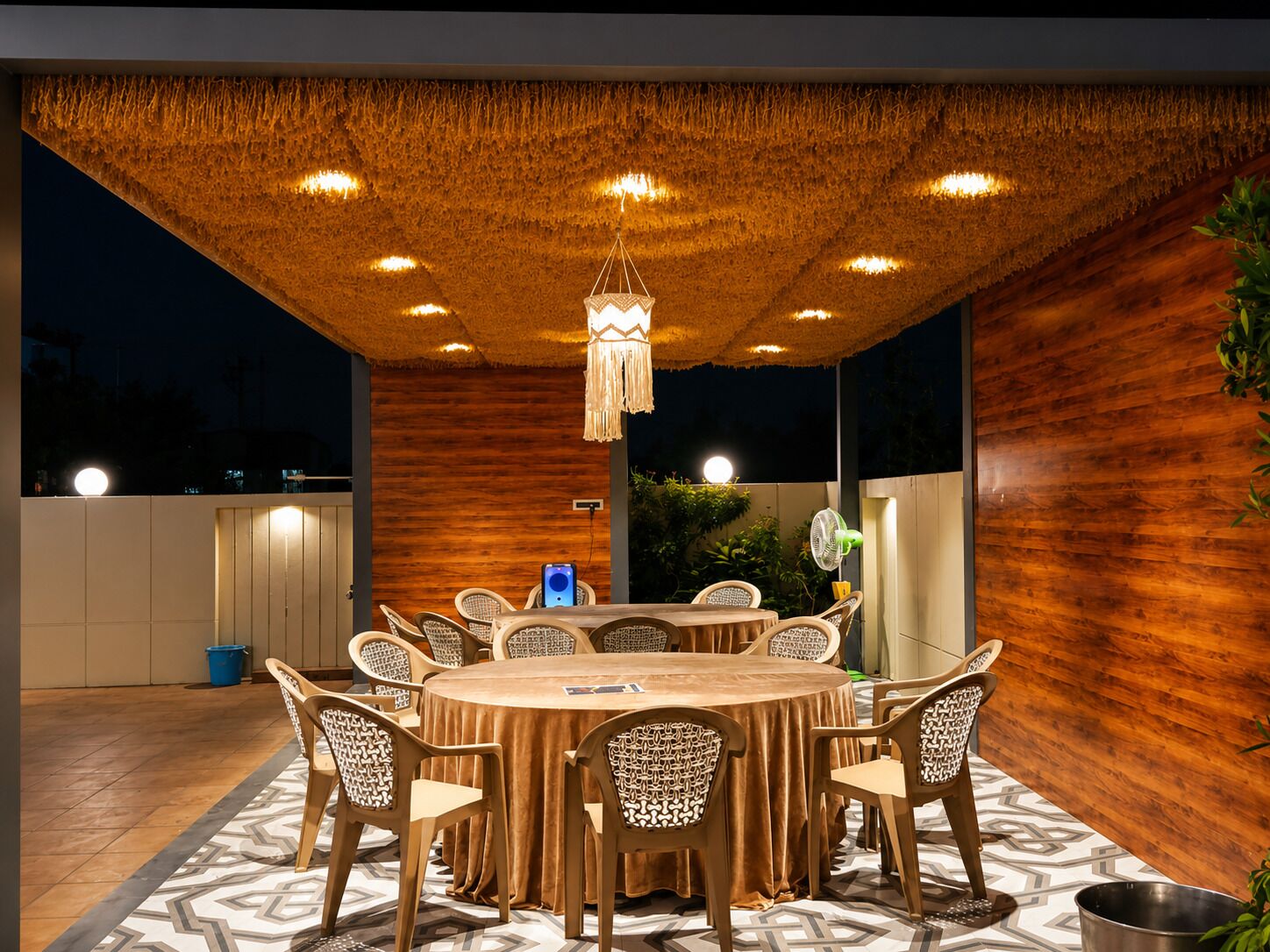 Uma área de refeições ao ar livre com uma mesa redonda, cadeiras e um lustre pendente.