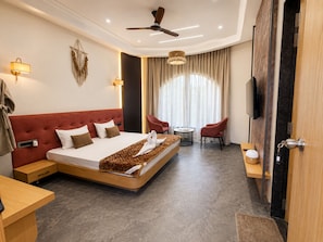 A hotel room with a large bed, a desk, a TV, and a ceiling fan. - Nakshatra Aura (Indore)