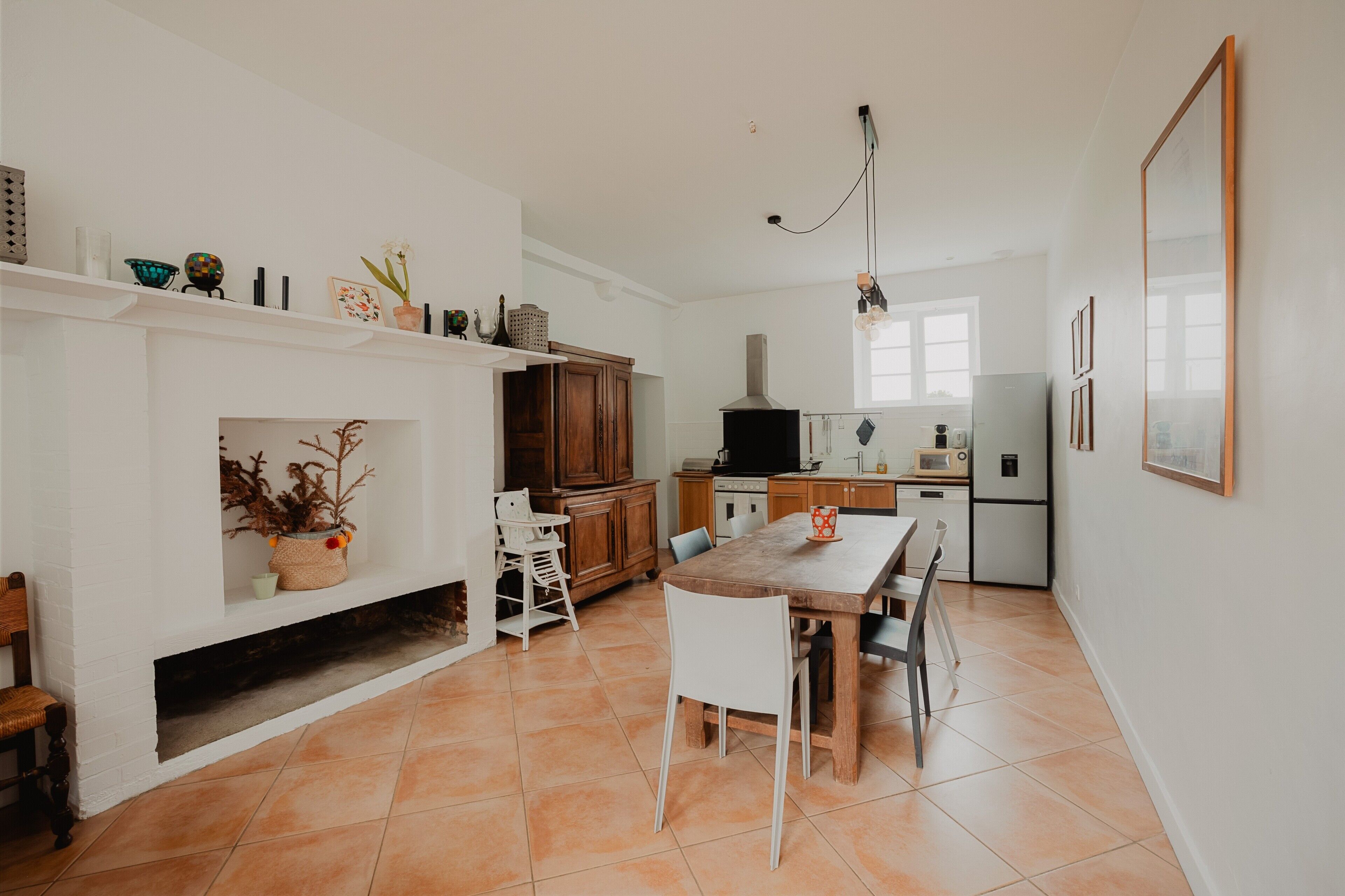 A modern kitchen with white walls, a wooden dining table, and a fireplace.