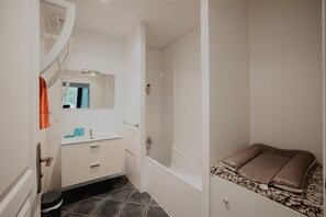 A bathroom with a bathtub, a sink with blue cups, a mirror, and a towel rack.