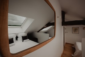 Ein Schlafzimmer mit Dachfenster, Holzbalken an der Decke, einem Bett und einem Spiegel.