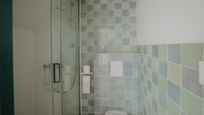 Et badeværelse med brusekabine i glas, toilet og væg med mosaikfliser.
