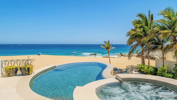 Ein Pool mit geschwungener Form, ein Whirlpool und Blick auf einen Strand.