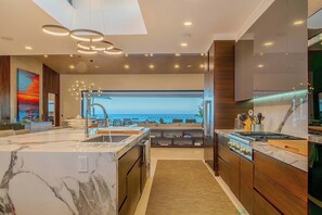 A modern kitchen with a large island, a view of the ocean, and a dining area with a view. - Casa Keller: Beachfront in Pedregal | 2 Swimming Pools (Cabo San Lucas)