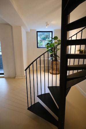 Un interior moderno con una escalera negra, un ventanal con vistas a la vegetación y una cesta de mimbre con una planta.