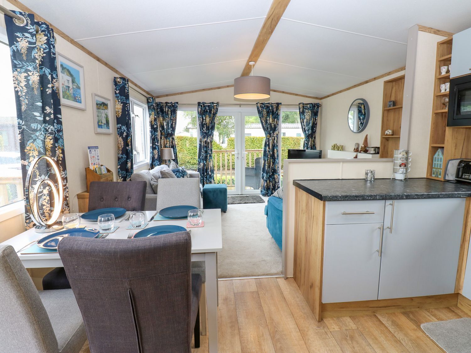 A modern kitchen with a central island, a dining area with a table set for two, and a living area with a sofa and a TV.