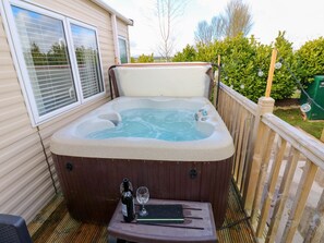 Ein Whirlpool mit einer Holterrasse, ein Tisch mit Flasche und Glas sowie ein Fenster mit Jalousien.
