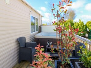 Un área de estar exterior acogedora con jacuzzi, rodeada de plantas en macetas y una terraza de madera.