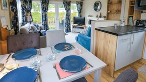 A compact living space with a dining area, kitchenette, and seating by a window with curtains. - Plot 41 (Carlisle)