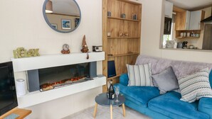 A living room with a fireplace, a blue sofa, a round mirror, and a wooden shelf with decorative items. - Plot 41 (Carlisle)