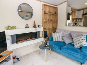 Ein Wohnzimmer mit Kamin, einem blauen Sofa, einem runden Spiegel und einem Holzboden mit Dekoration.