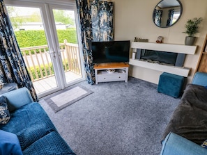 Ein Wohnzimmer mit Fernseher, Sofa und einem Balkon mit Vorhängen.