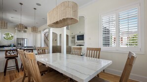 Uma sala de jantar com mesa de mármore, cadeiras de madeira e luminárias pendentes trançadas.