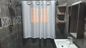A bathroom with a shower curtain, a handheld showerhead, a sink, and a mirror. - Heidi’s Beach Stay (Mombasa)