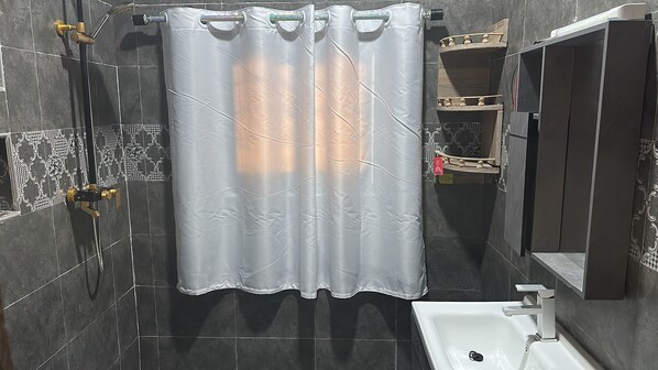 A bathroom with a shower curtain, a handheld showerhead, a sink, and a mirror.