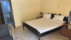 A bedroom with a bed, nightstands, a lamp, a chair, and a view of a bathroom. - Heidi’s Beach Stay (Mombasa)