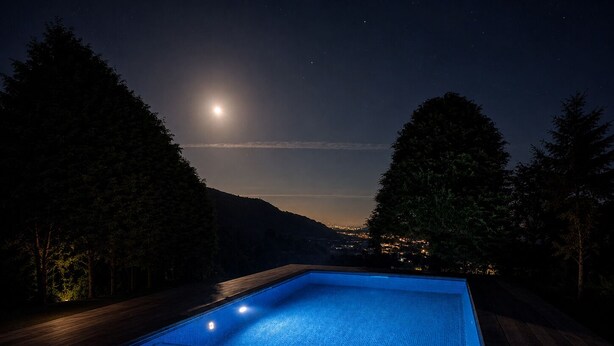 En rektangulær swimmingpool omgivet af en træterrasse, med en nattehimmel fyldt med stjerner og måne.
