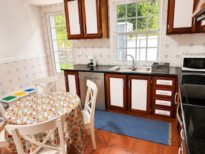 Une cuisine compacte dotée de meubles en bois, d’un évier à deux bacs, d’un four à micro-ondes et d’un coin repas avec une table et des chaises.