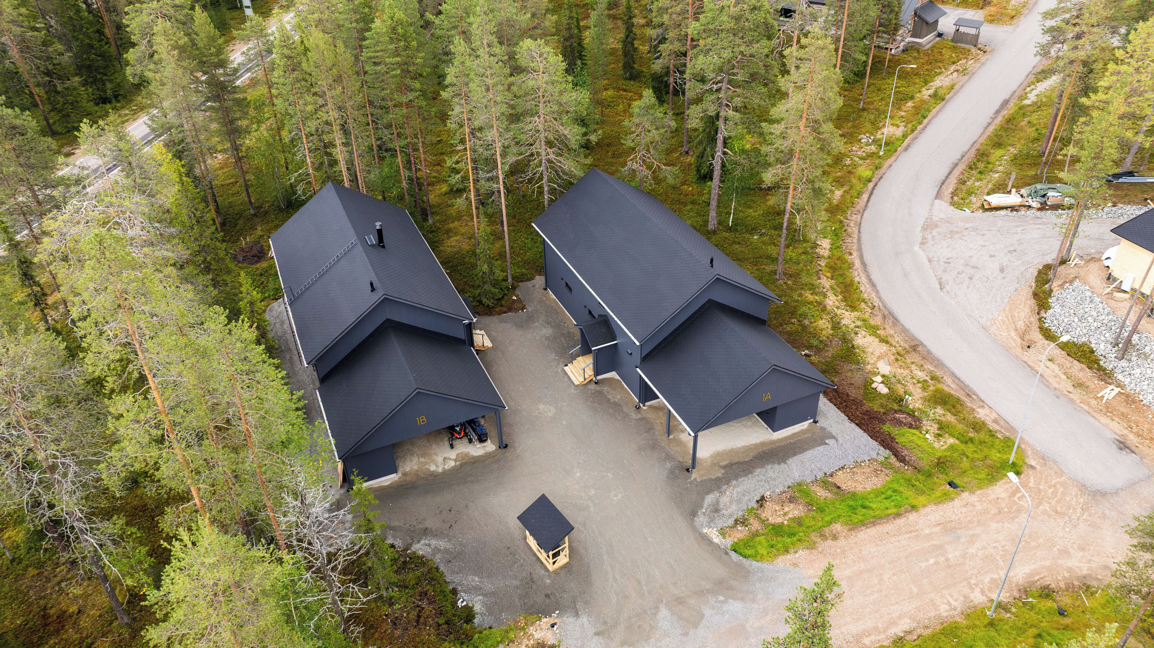 A residential area with two houses featuring dark roofs and a paved driveway.