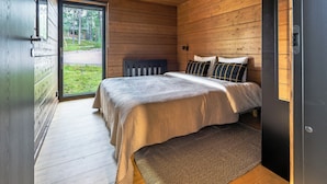 Un dormitorio con techo de madera, una cama con cabecera, una ventana y una puerta.
