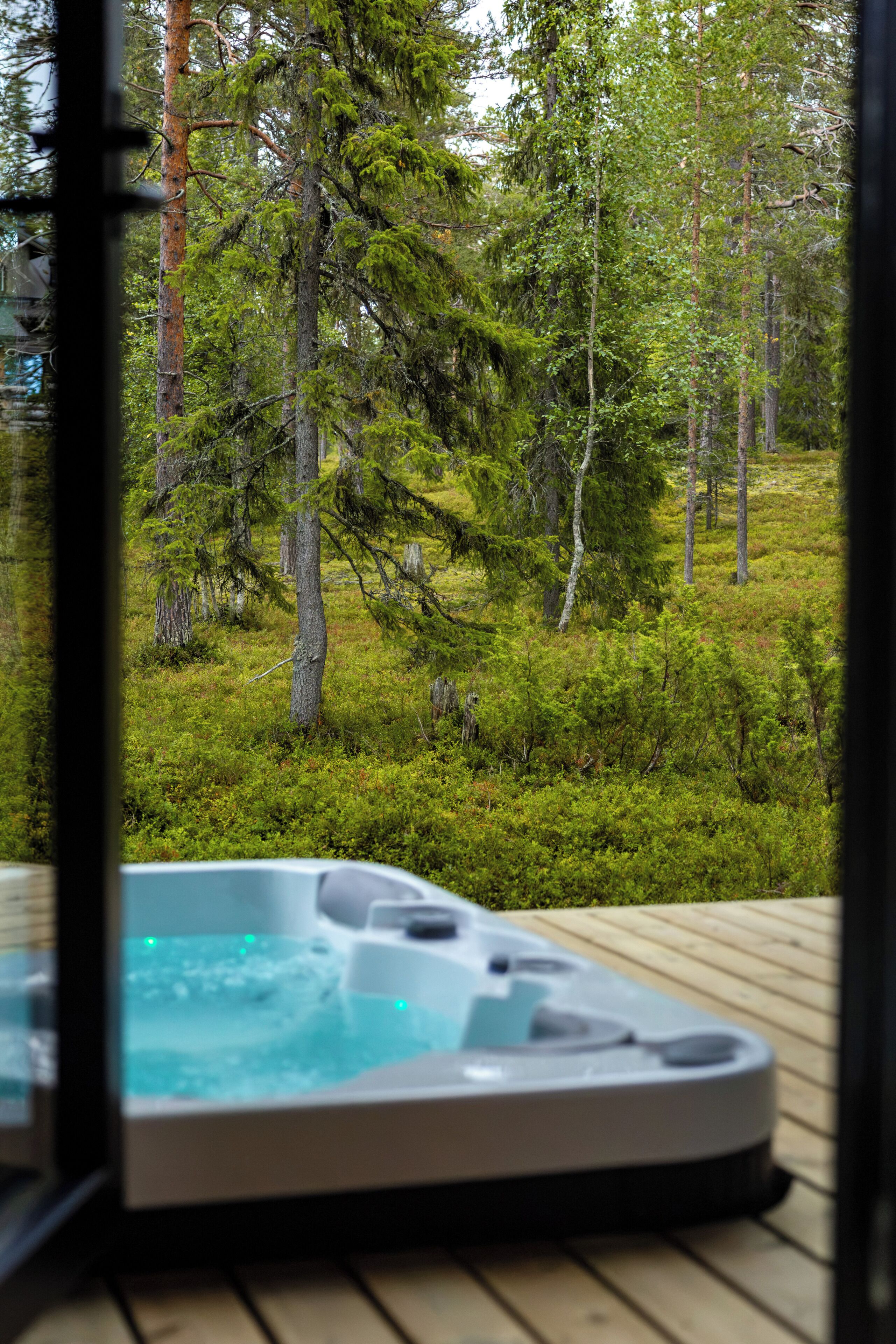 Een hottub op een houten terras met uitzicht op een bos.