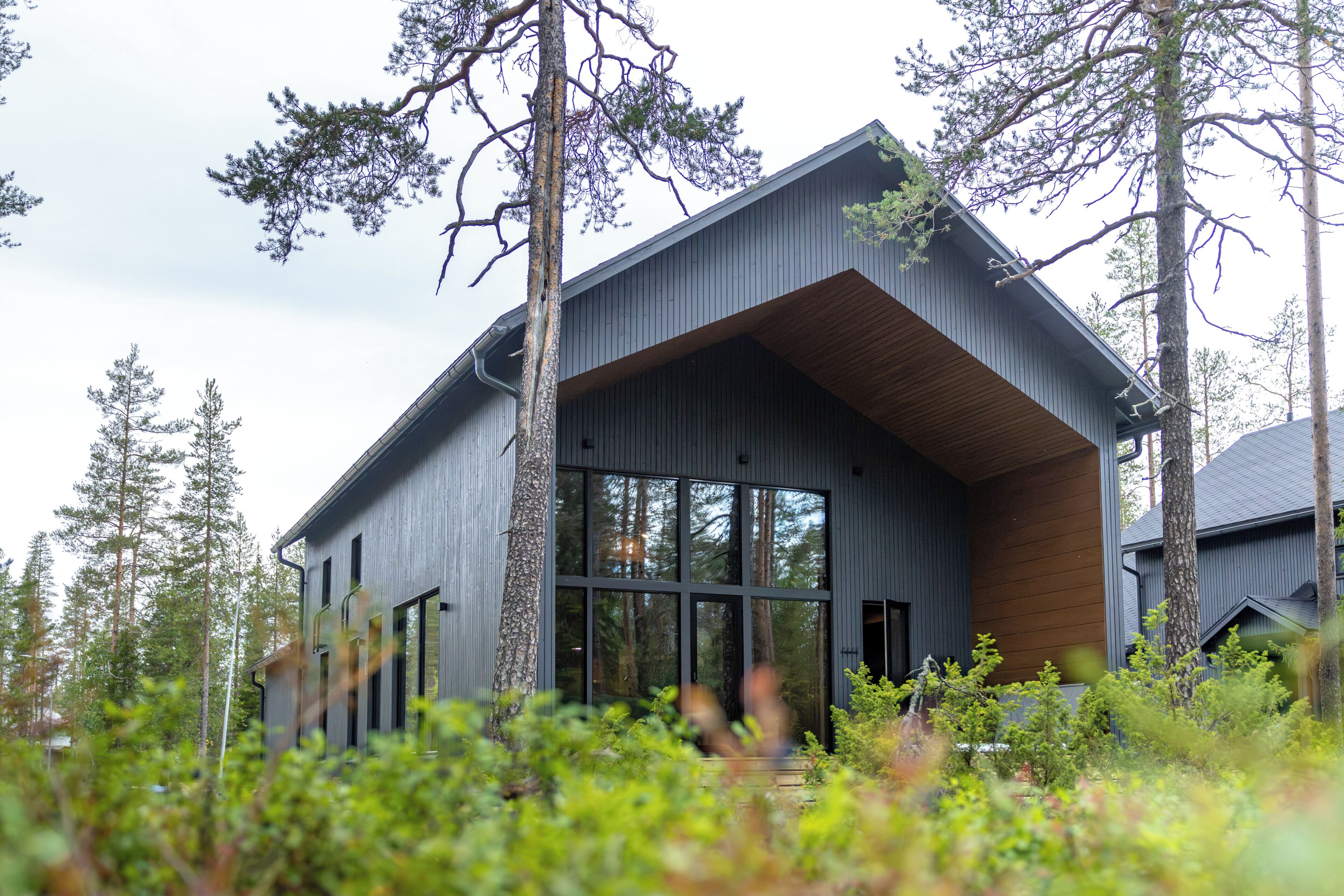 A modern house with a sloped roof, large windows, and a wooden overhang.