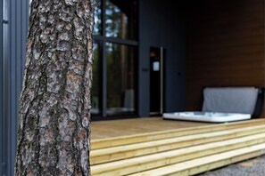 Una terraza de madera que conduce a un edificio moderno con puerta de vidrio y un sofá.