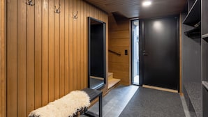 Un pasillo con paneles de madera, un banco con un cojín mullido, una puerta con marco negro y una escalera que conduce a otra habitación.