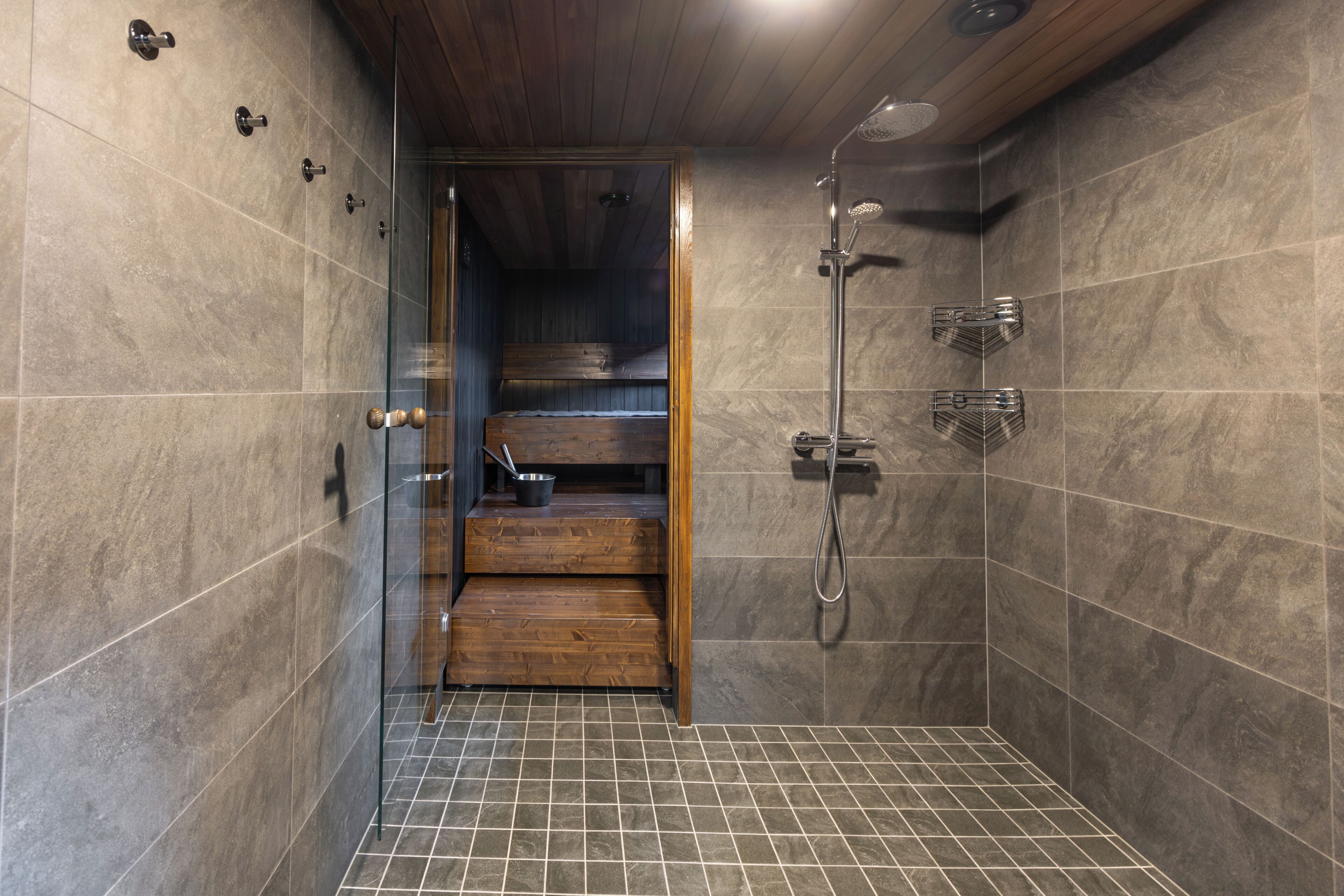 A modern shower area with a glass door, wooden steps, and a tiled floor.