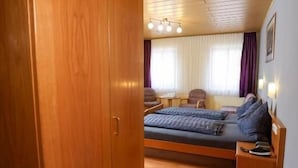 Une pièce comprenant une armoire en bois, un lit avec un matelas bleu, une table de chevet et une fenêtre avec des rideaux.