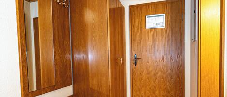A hallway with wooden floors, a bench, a door with a sign, and a mirror on the wall.